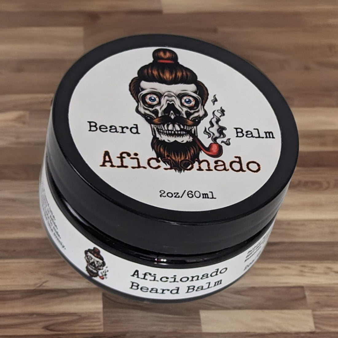 Aficionado beard balm in a black screw-top tin on a pale wood table