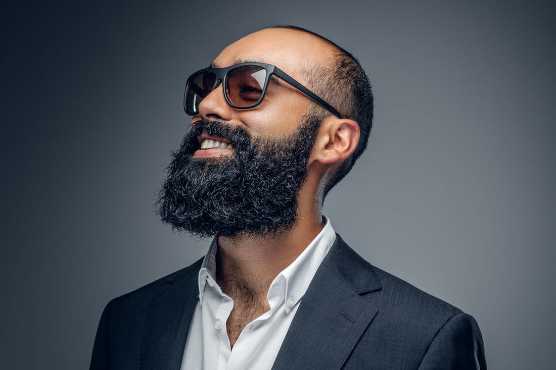 Fashion portrait of a bearded man in a suit and sunglasses on a grey background